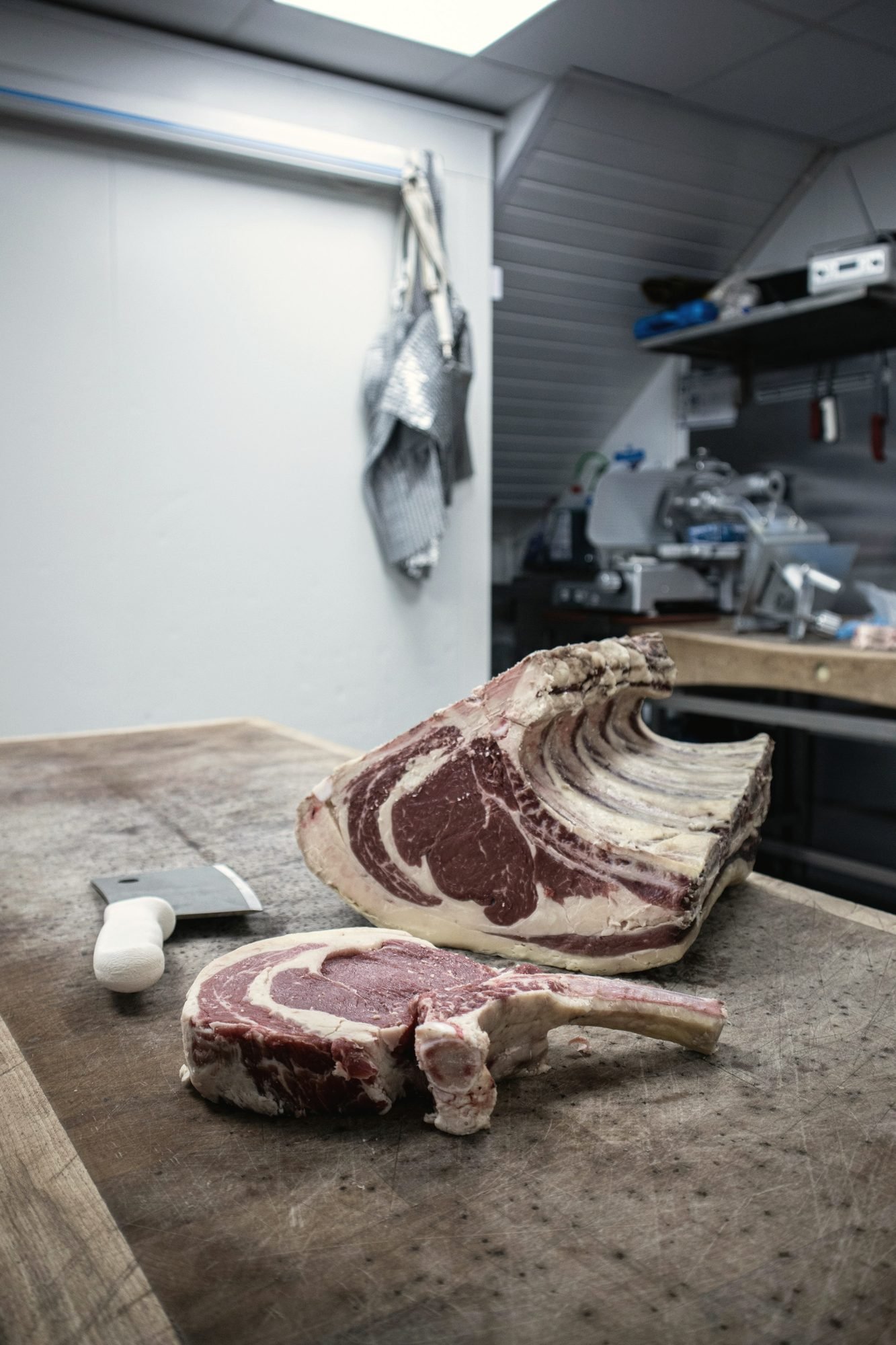 A beef rib section and a cut tomahawk steak on a butcher block in a cutting room