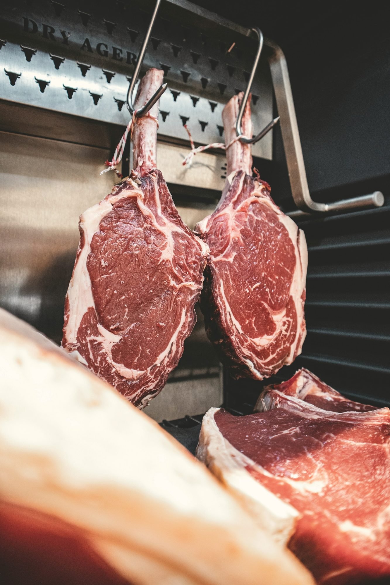 Beef rib sections hanging from hooks inside a walk-in cooler