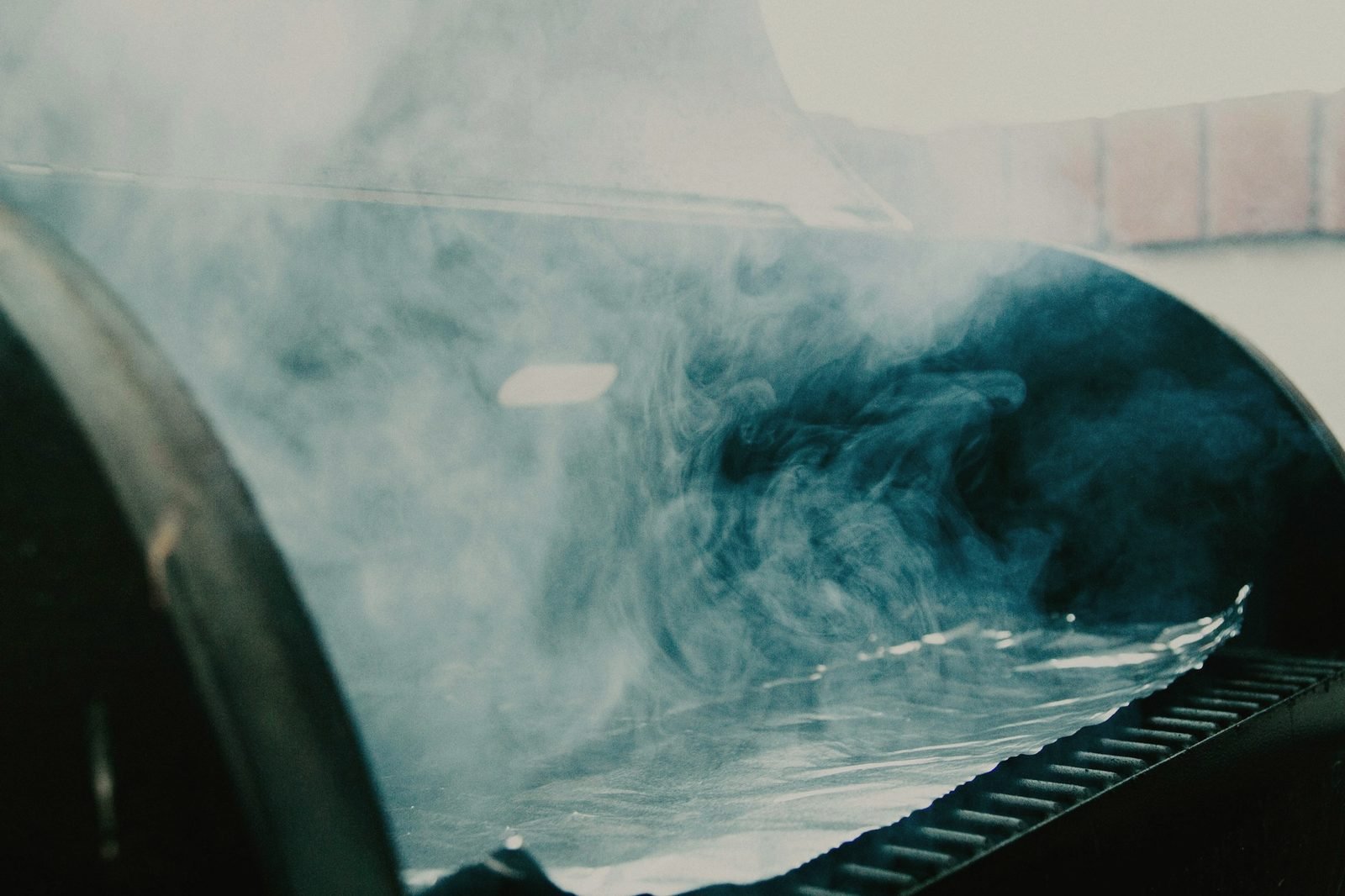 Smoke rolling out from under the lid of a backyard smoker