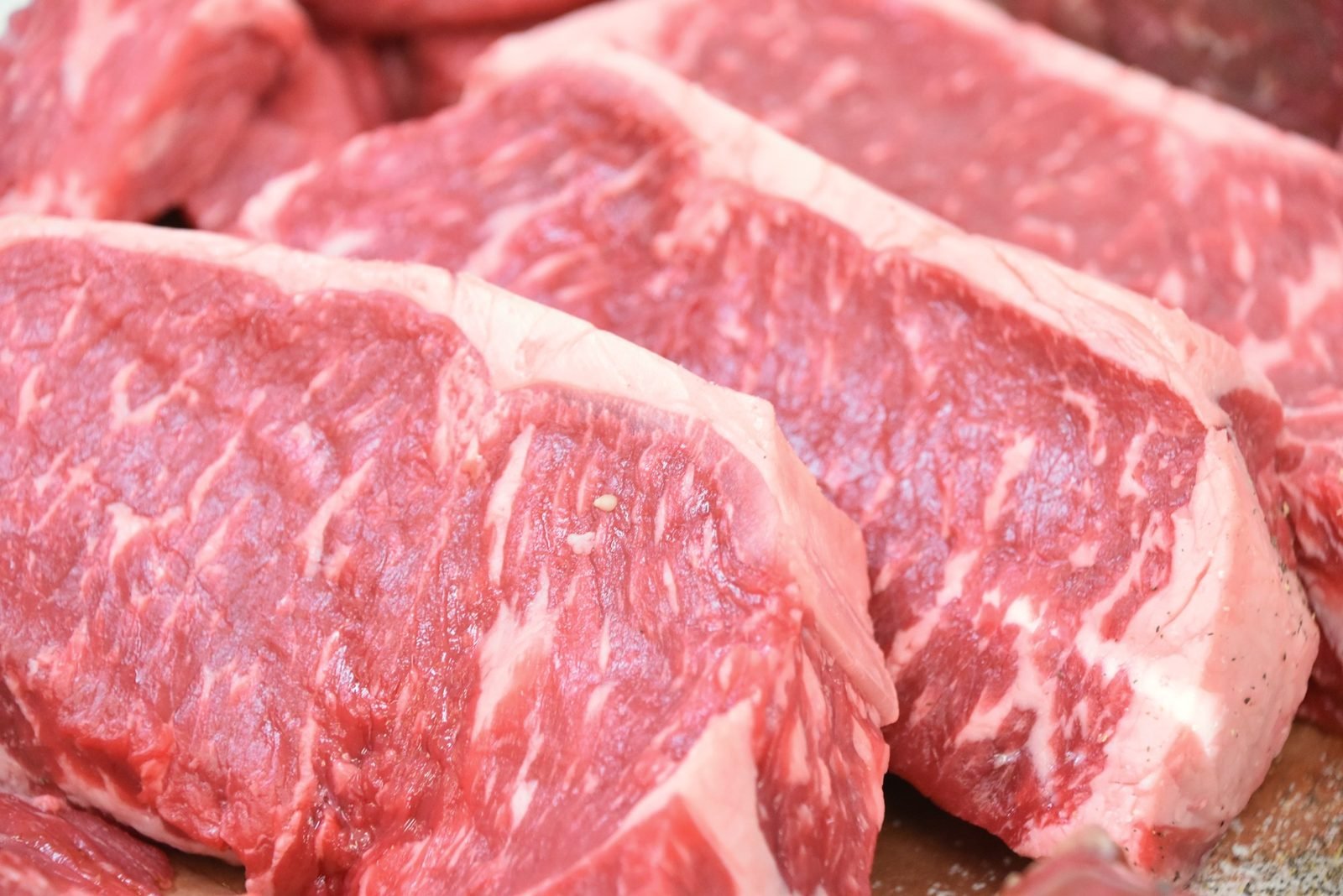 Close view of well-marbled raw strip steaks stacked together