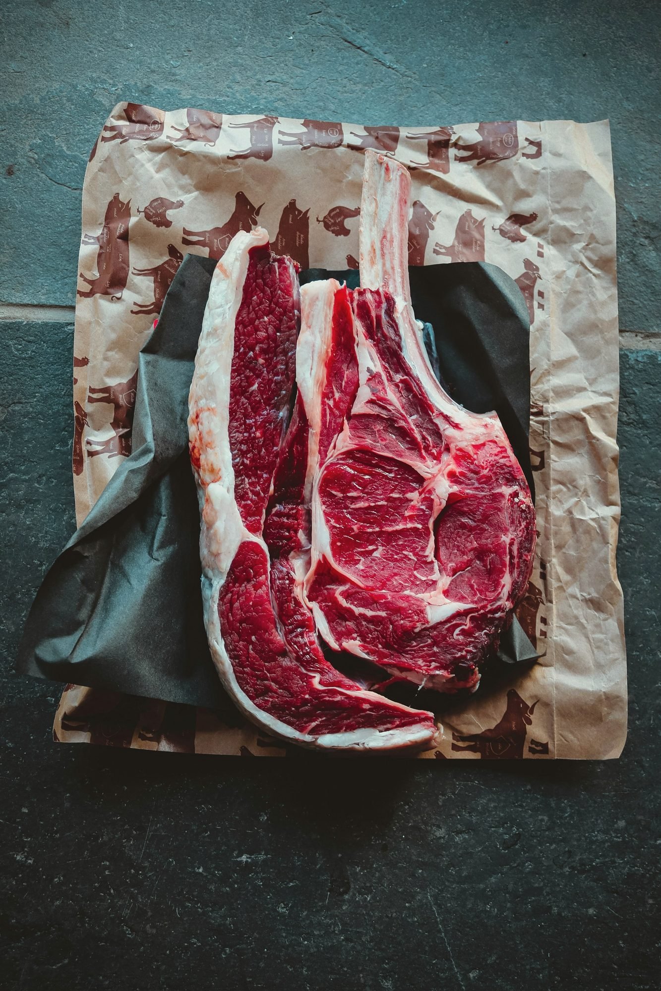 Two bone-in tomahawk ribeyes laid out on brown paper